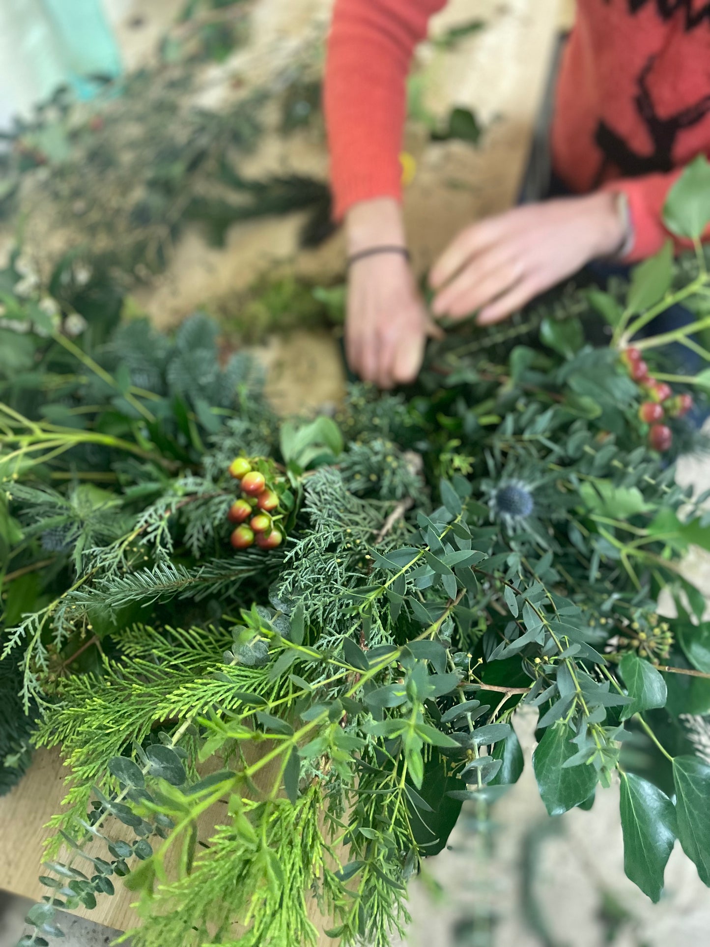 Person working with greenery and berries on a wreath-making workshop.